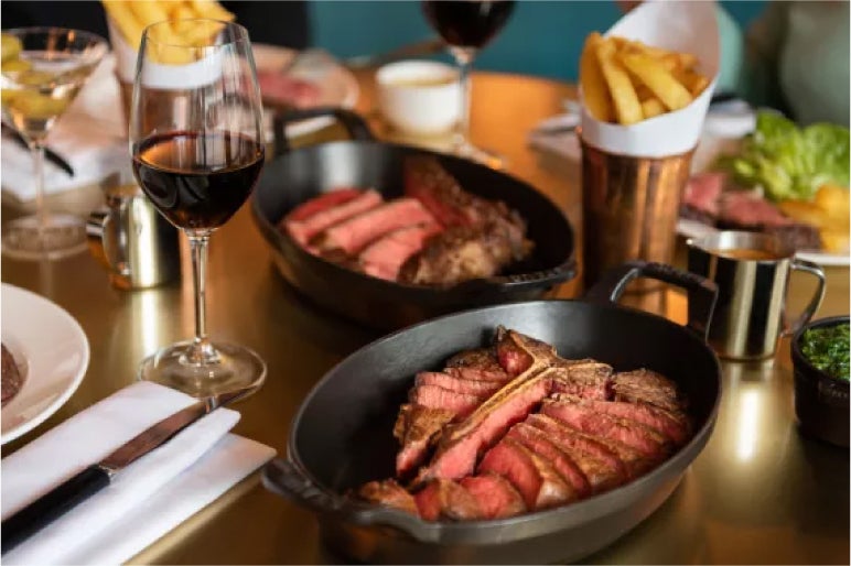 Steak slices in cast iron pans with fries, red wine, and condiments, served at Hawksmoor Borough Market