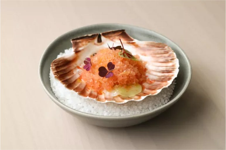 Scallop on sea salt, topped with granita and microgreens, a refined dish blending freshness and elegance in every detail