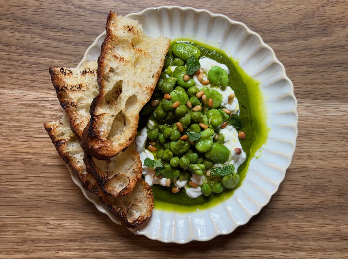 A delicious plate of burrata topped with vibrant green legums and slices of fresh toasted bread