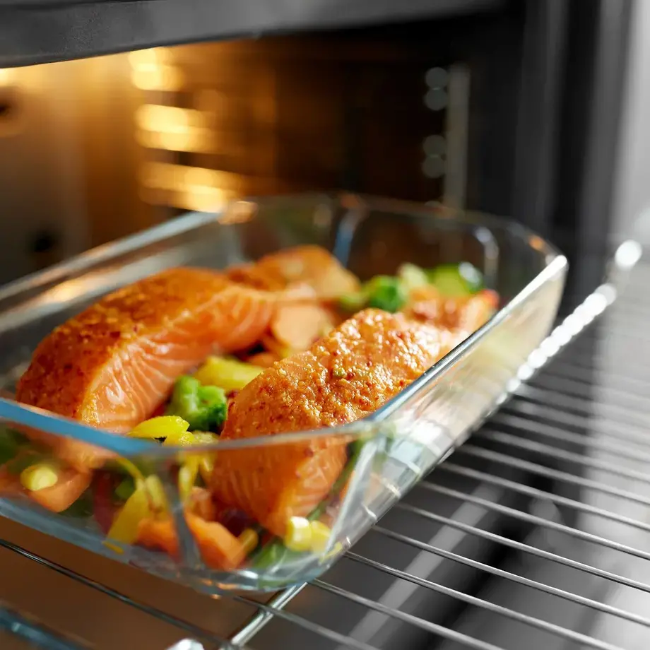 An ovenware dish containing two salmon fillets set on vegetables entering oven