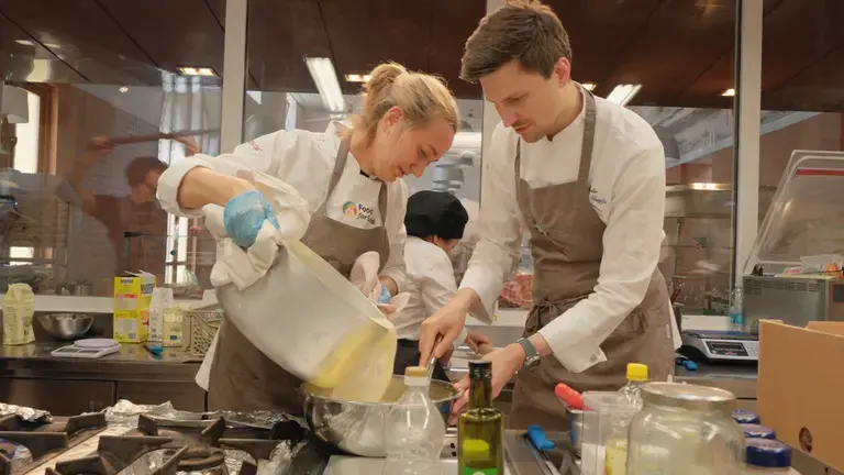 Chefs collaborating in a professional kitchen, pouring batter into a bowl