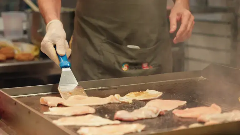 Chef grilling chicken breast on a professional griddle
