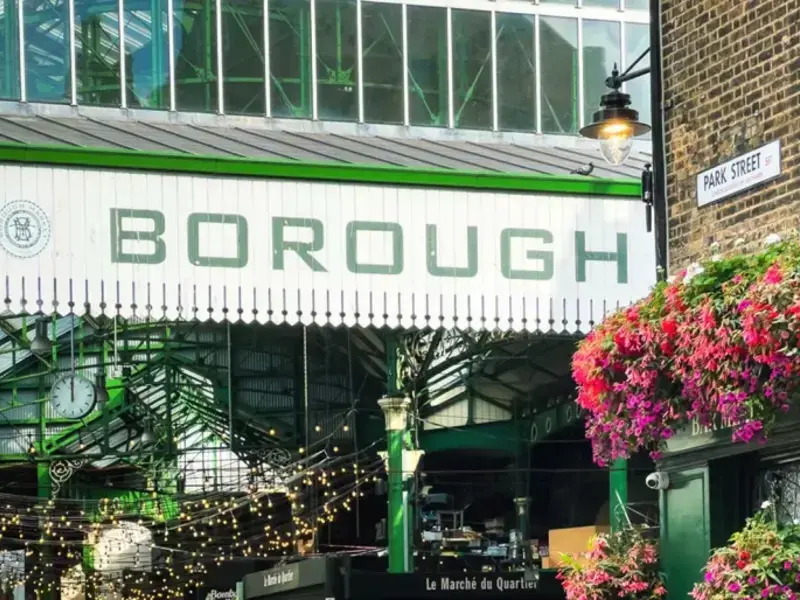 Entrance to Borough Market, London, adorned with lights and vibrant flowers, a hub for food lovers and fresh produce seekers