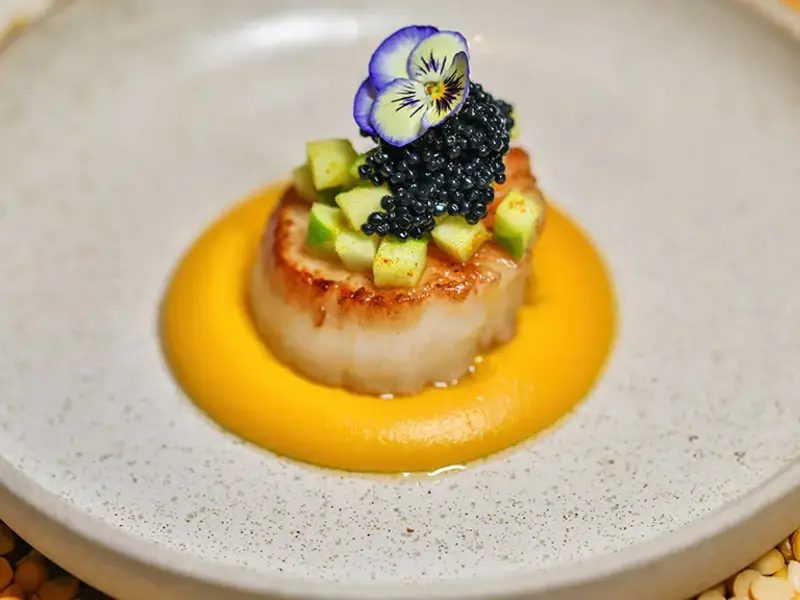 Gourmet scallop dish with edible flower and caviar garnish.