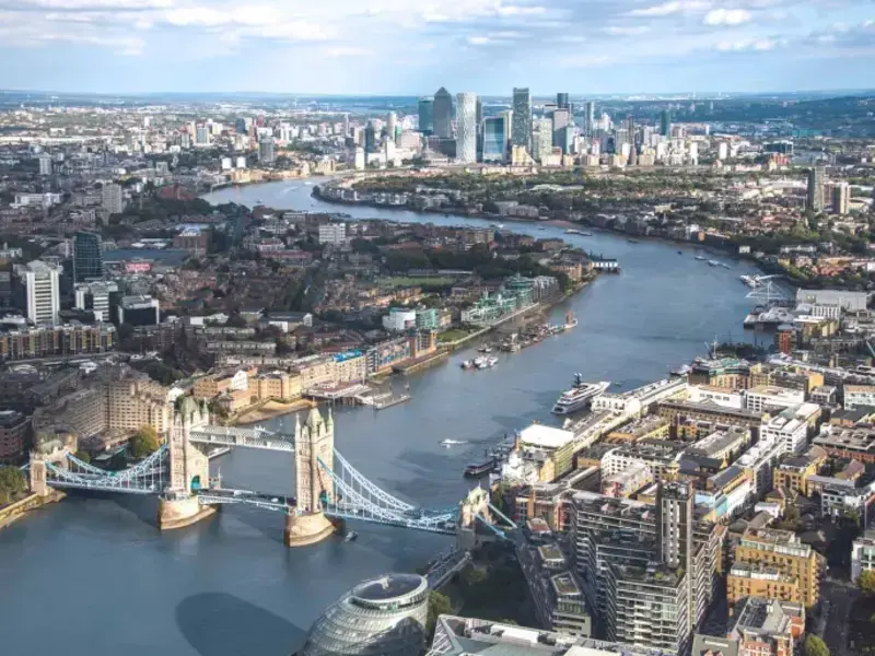 Aerial view of London featuring the iconic Tower Bridge, Thames River, and modern cityscape of Canary Wharf in the background
