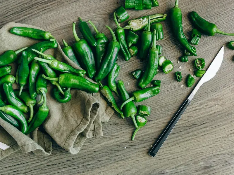 A chopping board and knife with green whole and sliced jalapeno peppers