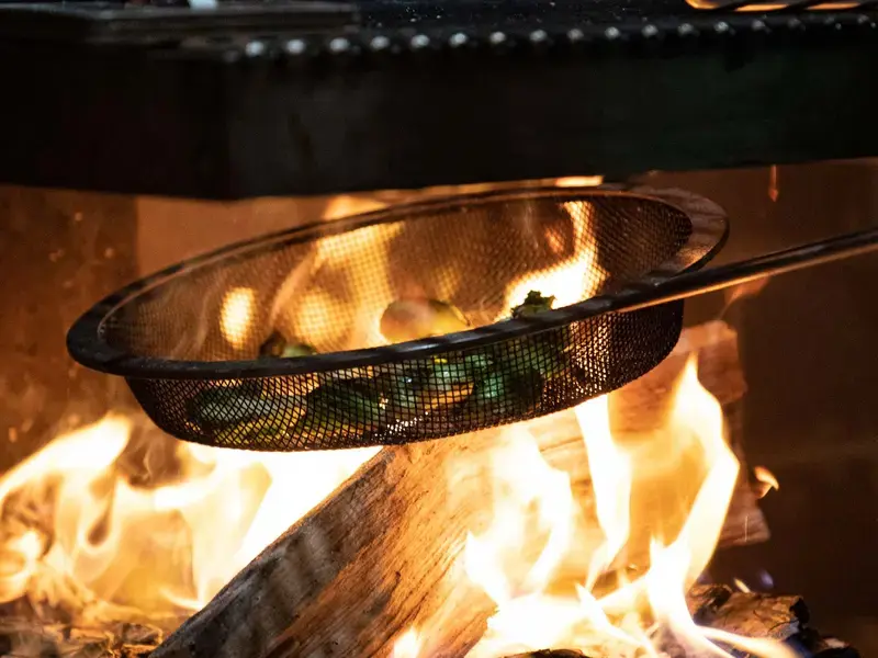 A grill pan above a fire with vegetables on in