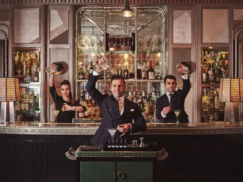 Three people mixing drinks at a bar.
