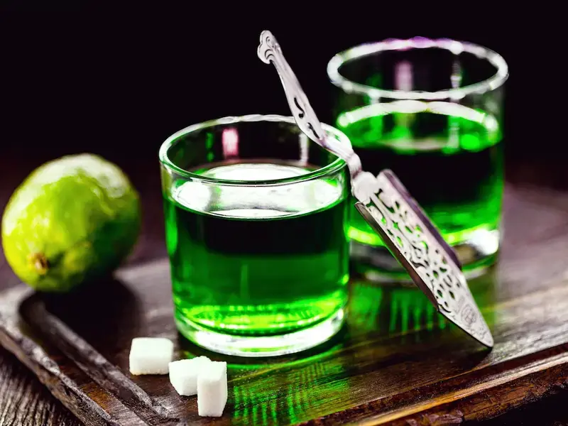 Two glasses of absinthe with sugar cubes and lime on the side.