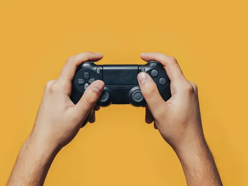 Two hands holding a videogame controller on a yellow background