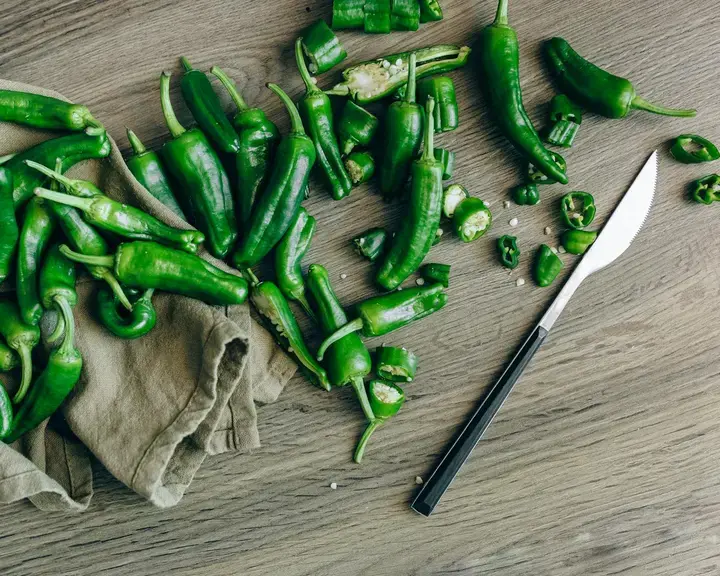 A chopping board and knife with green whole and sliced jalapeno peppers